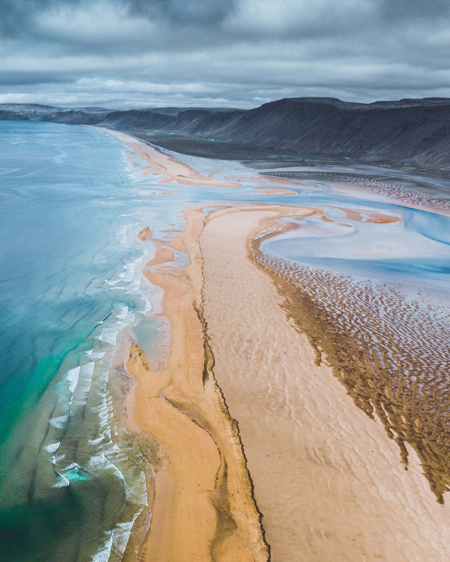 Aerial view of a coastal landscape with a long sandbar and blue water.